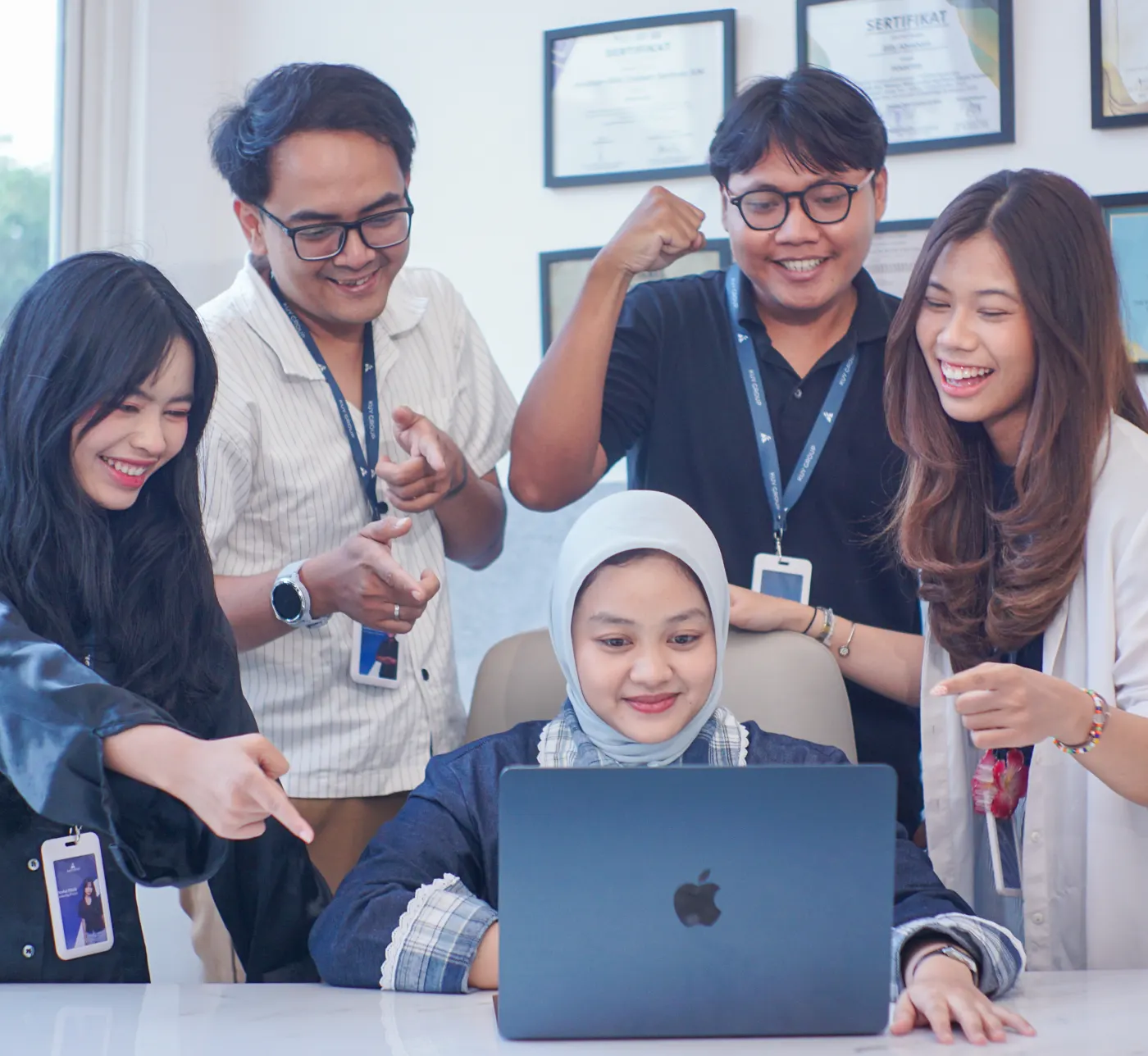 Five Kuy Studio team members gathered around a laptop, smiling and cheering