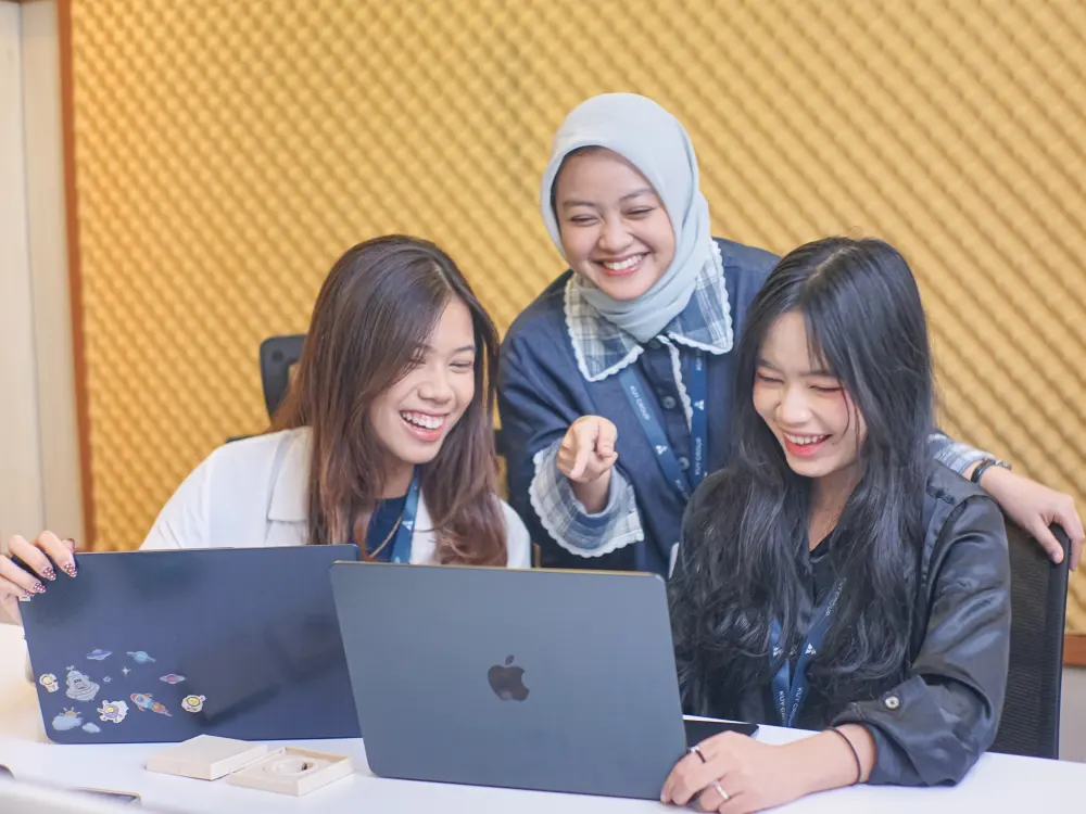 Three Kuy Studio teammates laughing together around a laptop