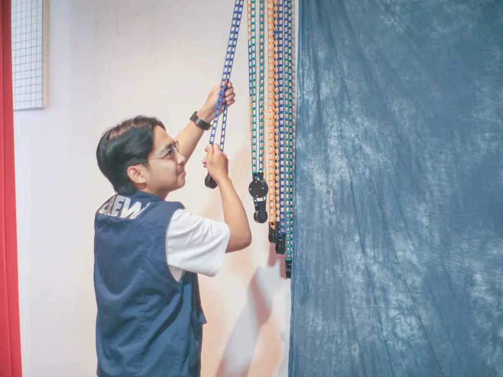 A studio crew member adjusting the backdrop chains before a session